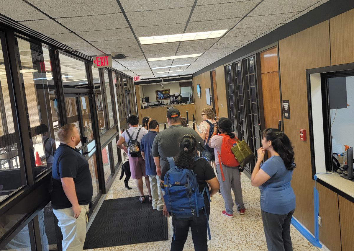 A group of adolescents stand in a hallway. Some are wearing backpacks and carrying canes; one has a guide dog.