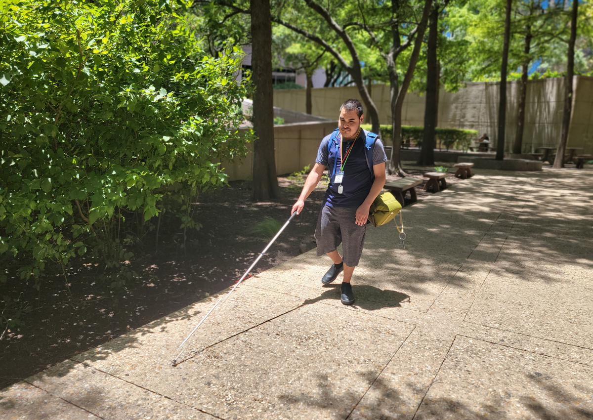 An adolescent wearing a backpack uses a cane to walk to work.