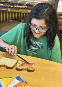 Un(a) estudiante utiliza un cuchillo para untar gelatina en el pan.