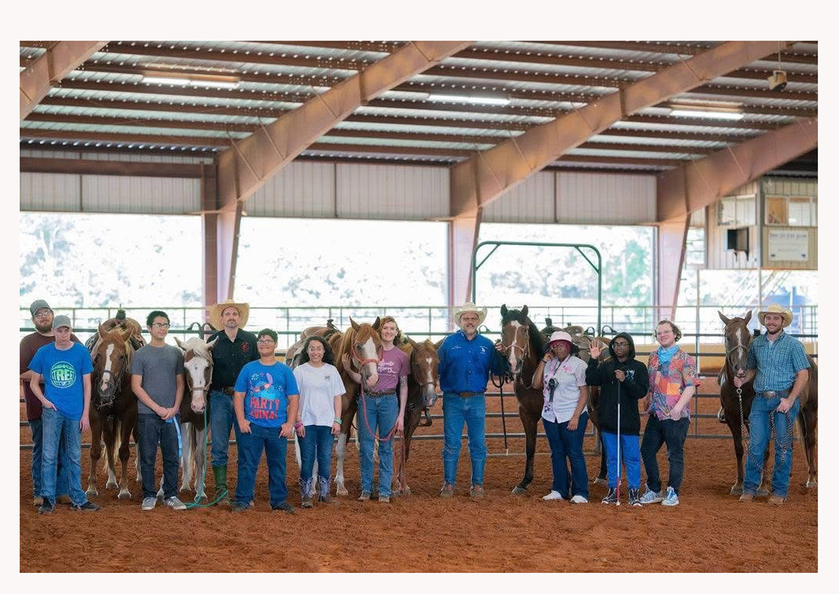 Estudiantes y adultos parados junto a caballos en un área cubierta.