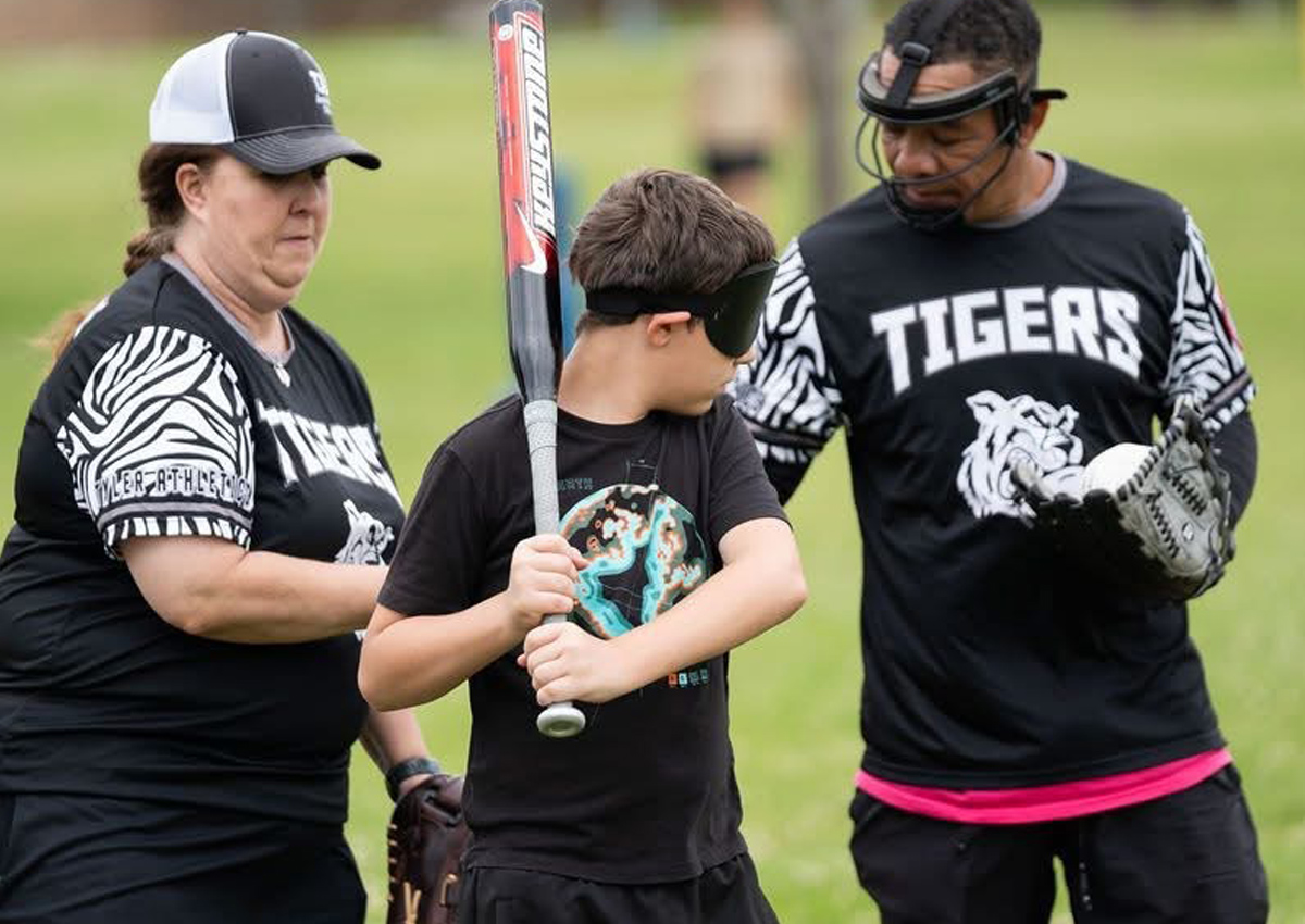 Un estudiante con los ojos vendados recibe instrucciones para batear.