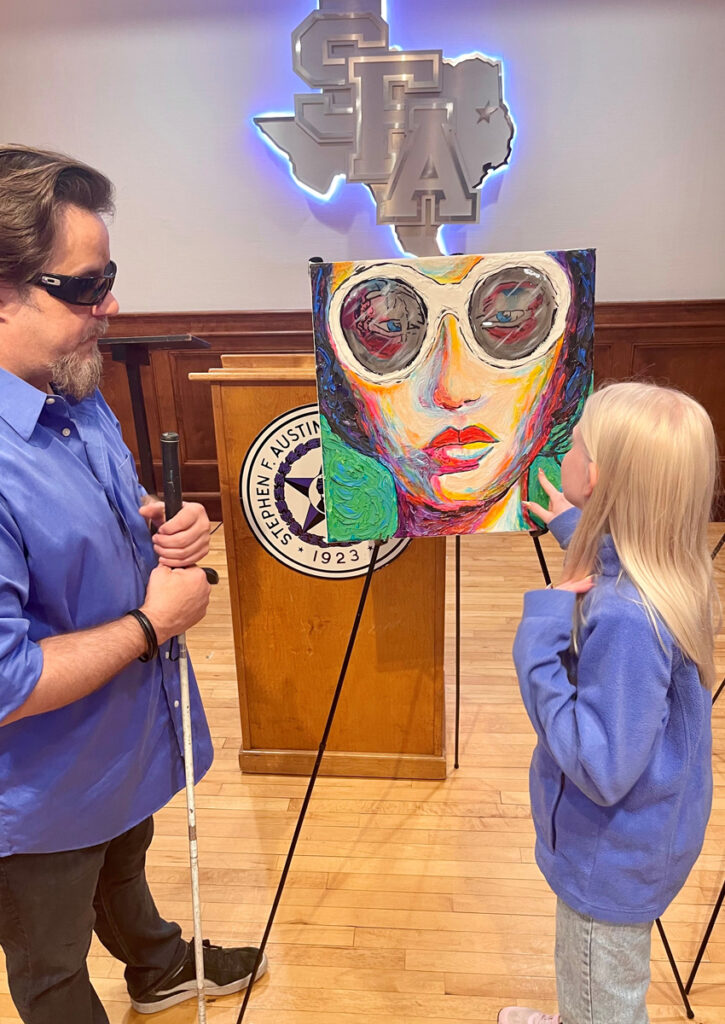 Una estudiante toca una pintura de un rostro con gafas grandes y colores intensos.