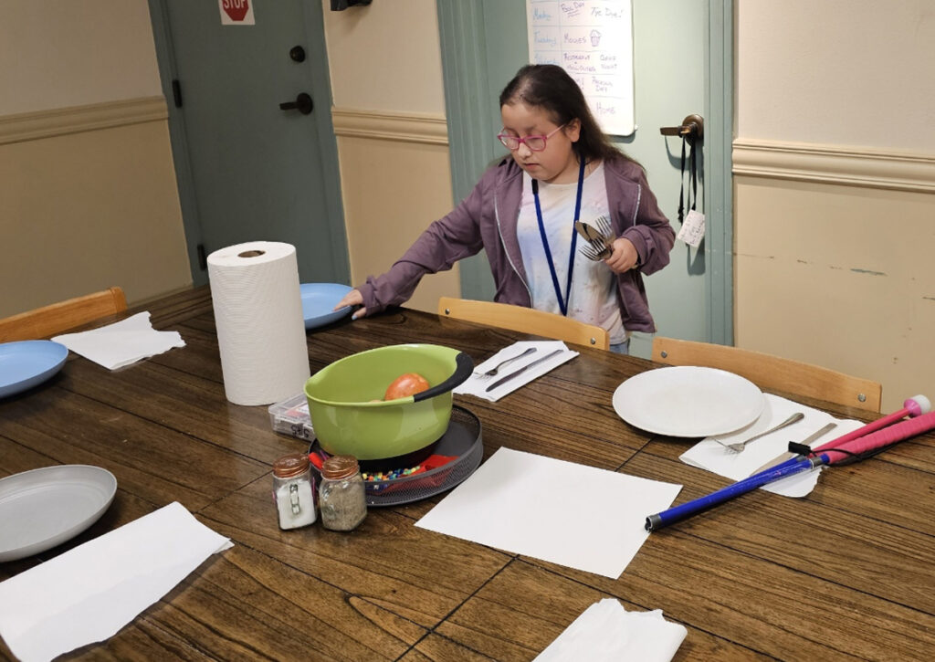 An adolescent sets a table for four.
