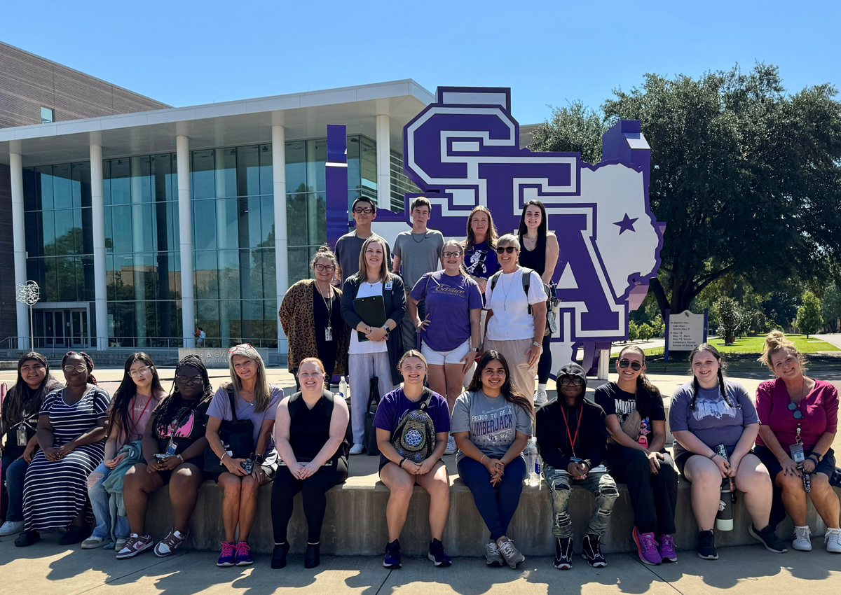 Students pose next to the purple and white SFA Texas sign.