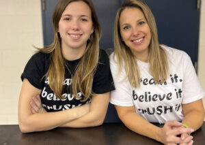Two women smile side by side in matching “Dream it. Believe it. CRUSH it.” shirts.