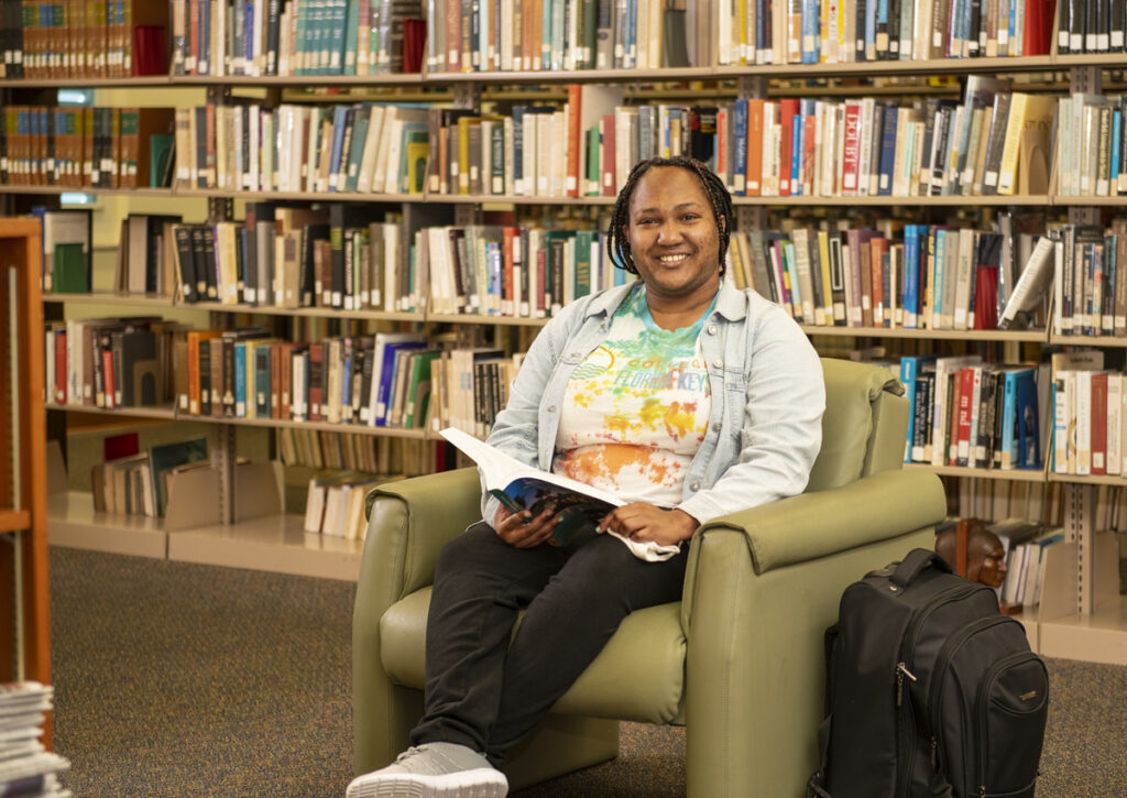 A student smiles as she enjoys reading a book in the campus library.