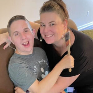 A smiling woman hugs her son, who holds a paintbrush in his hand.