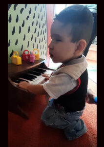 Un joven estudiante se arrodilla frente a un pequeño piano para tocar las teclas.