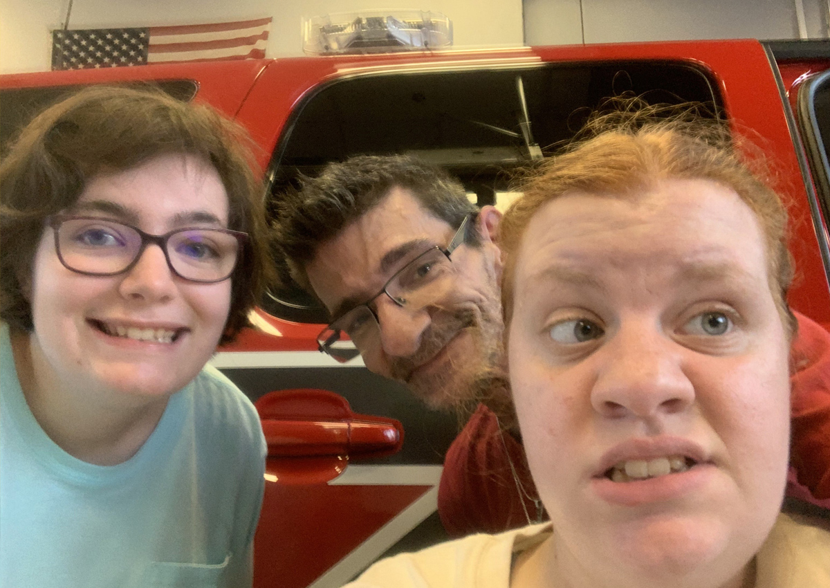 Three adults pose in front of a fire truck.