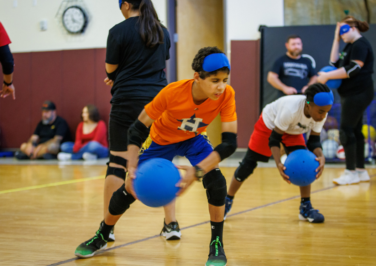 Two students hold goalballs, preparing to throw. Both have goggles on the top of their heads.
