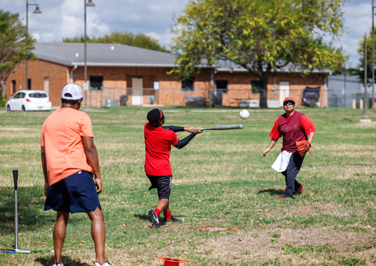 The pitcher and catcher watch as a young student hits the beeping baseball.
