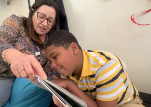 Smiling adolescent leans close and touches the book with a favorite reading partner in close proximity.