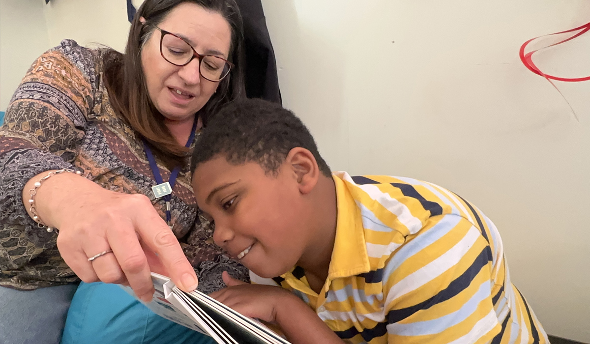 Smiling adolescent leans close and touches the book with a favorite reading partner in close proximity.