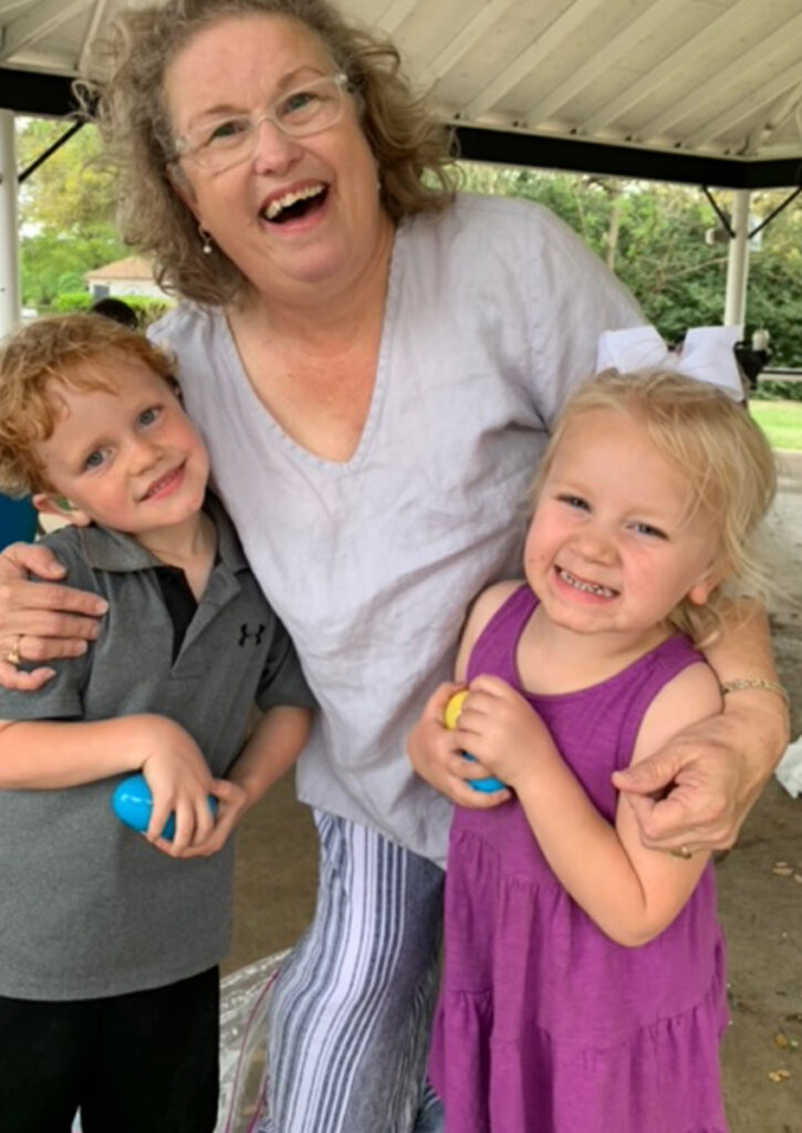 A woman laughs while hugging two young children under a pavilion.