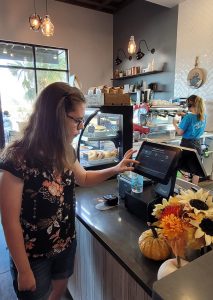 A young woman uses the fingers on her left hand to select items on the screen at the coffee shop.