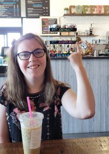 A young woman has a big smile as she points to coffee signs on the wall behind her.