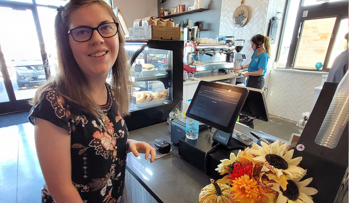 A young woman smiles when standing in front of the register.