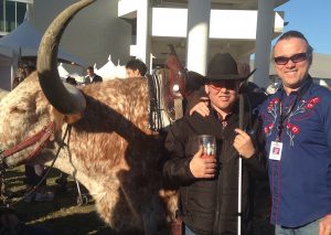 An adolescent and adult stand next to a longhorn bull at an outside event.
