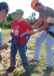 Two staff members at Camp Villa help a young man put on the harness for the zipline.